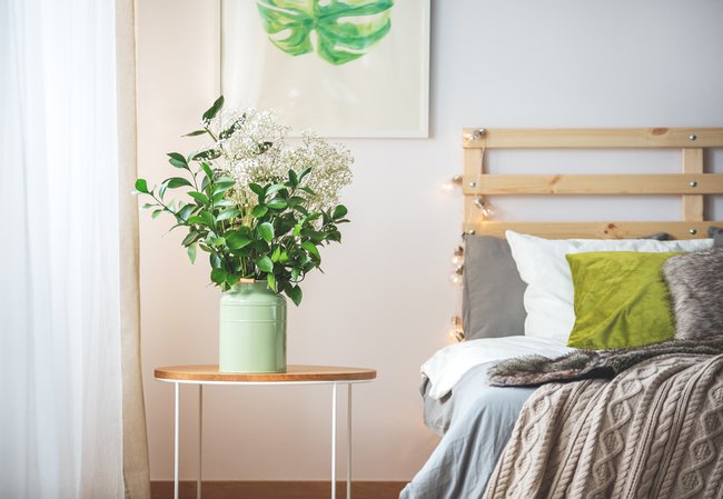 Bunch of flowers on small table next to bed in cozy bright bedroom